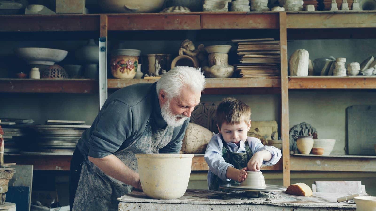 Elderly craftsman teaching a young boy on a pottery wheel in a workshop — business succession and knowledge transfer
