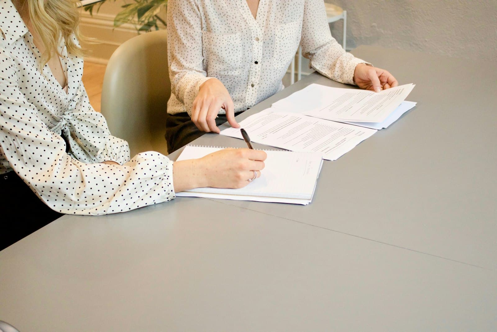 Two women reviewing and signing legal documents at a table in a bright modern office — contesting a will in Texas