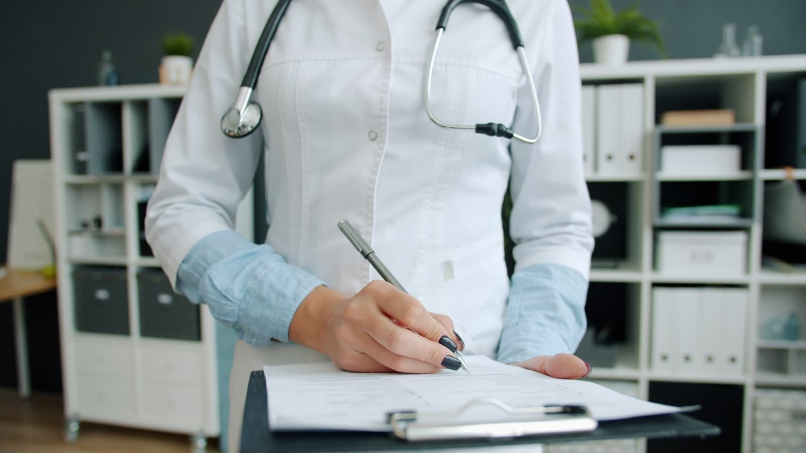 Healthcare professional in white coat with stethoscope writing on a clipboard in a clinical office — Medicaid in Texas
