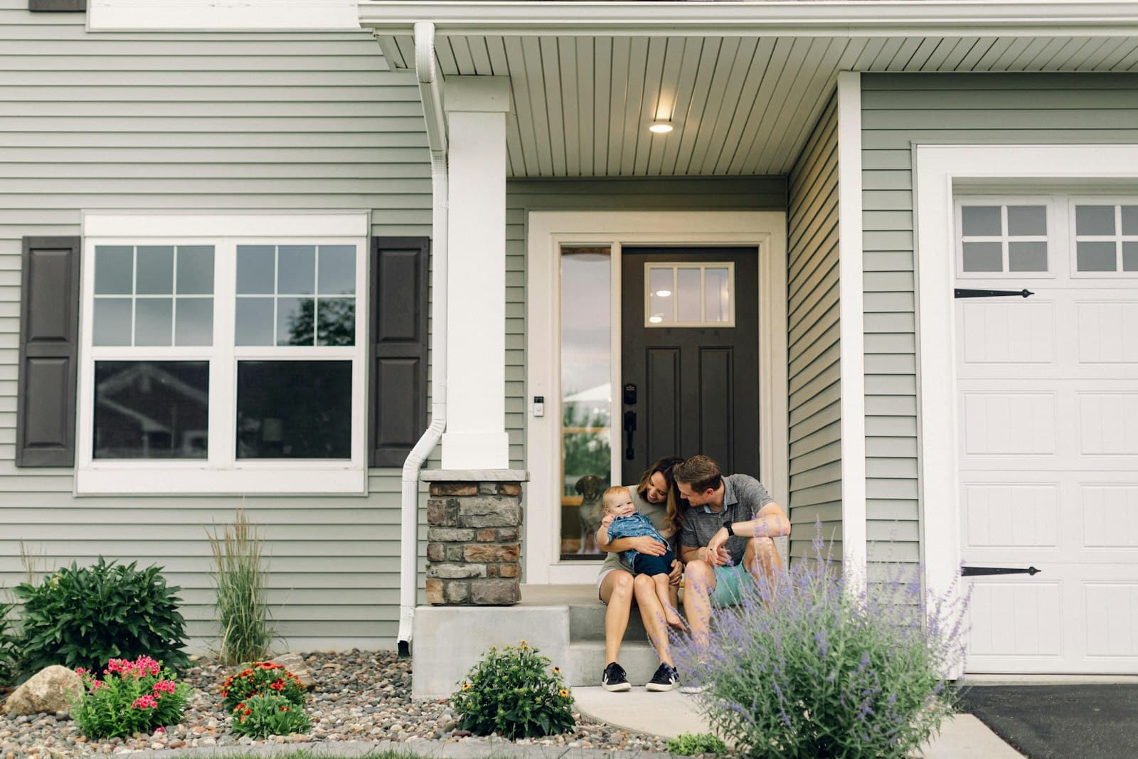 Young family with infant sitting on their front porch steps under the covered entry of their home