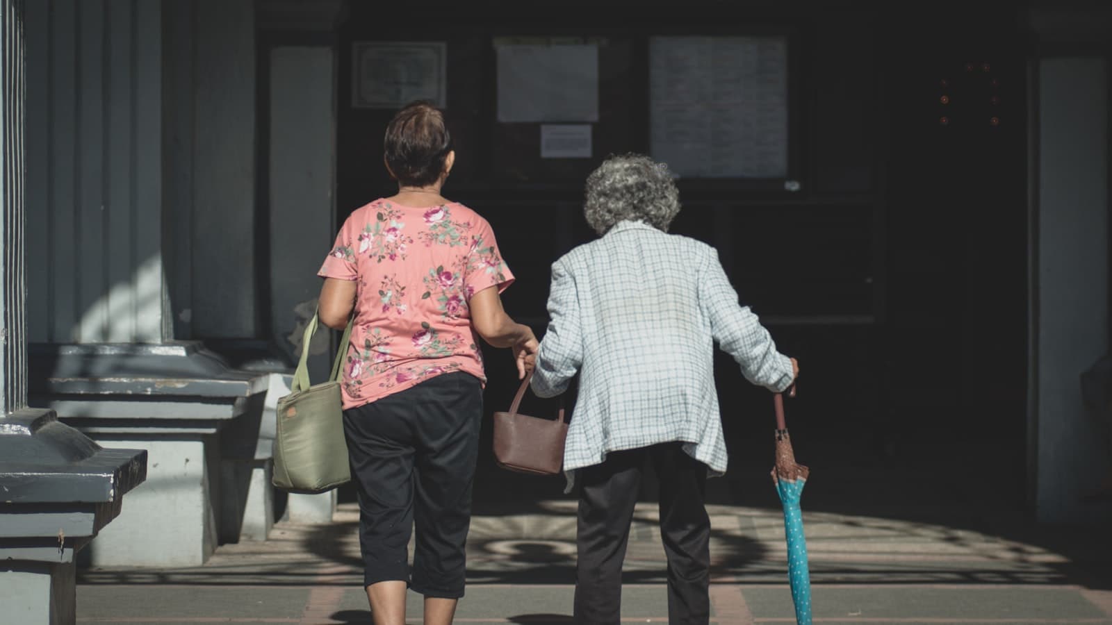 Caregiver accompanying an elderly woman toward a care facility entrance — Medicaid crisis planning in Texas