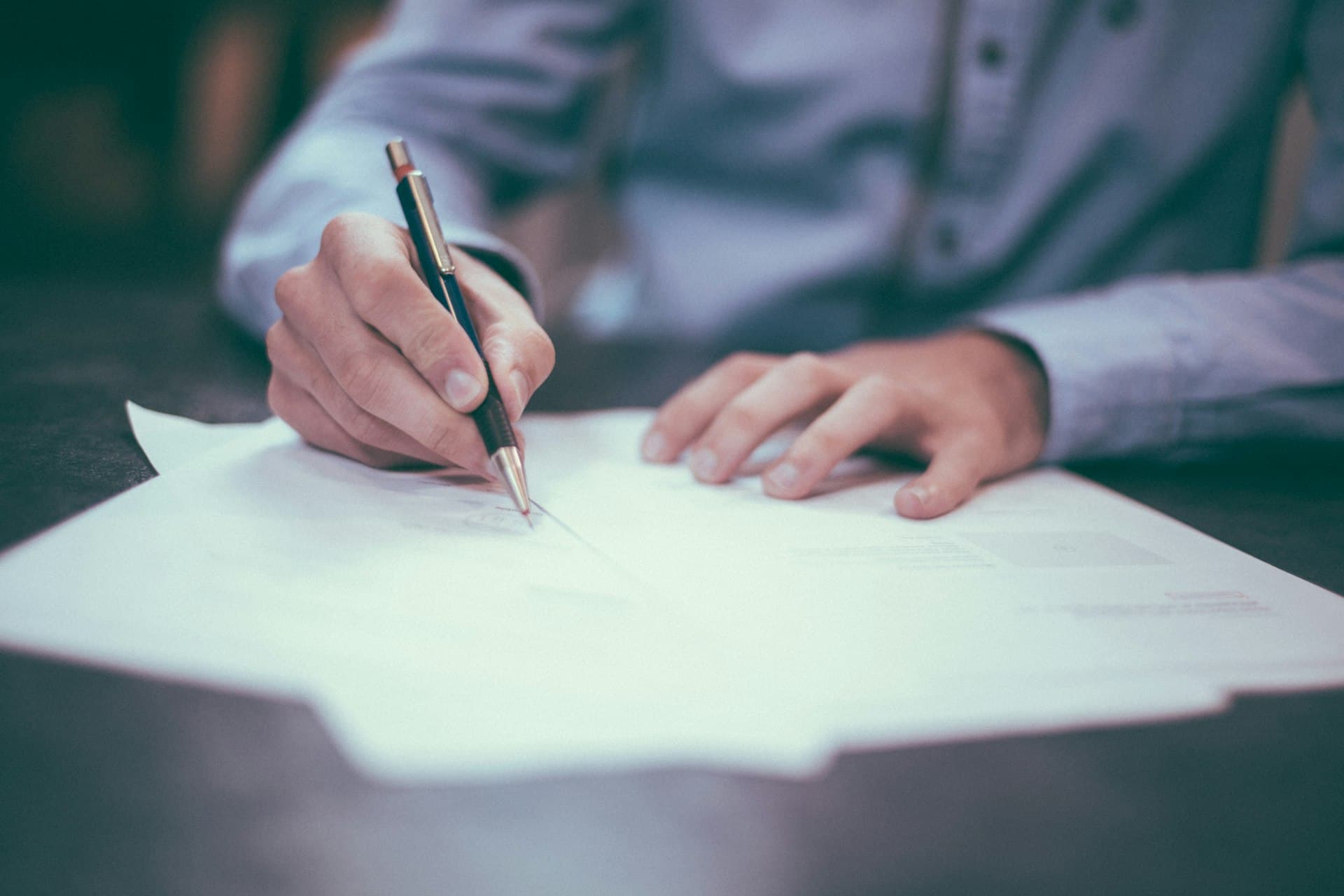 Close-up of a hand signing legal documents with a pen on a dark desk — estate plan execution