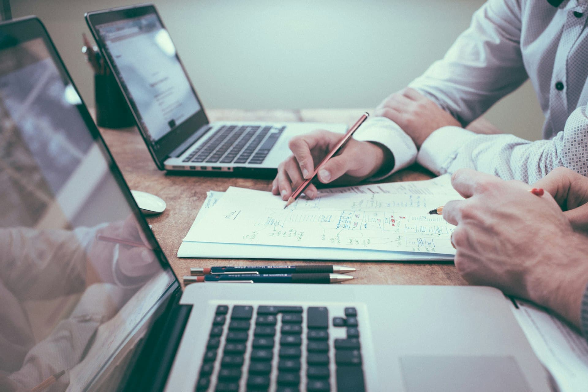Two business partners working through an agreement together at a shared table with laptops and notes