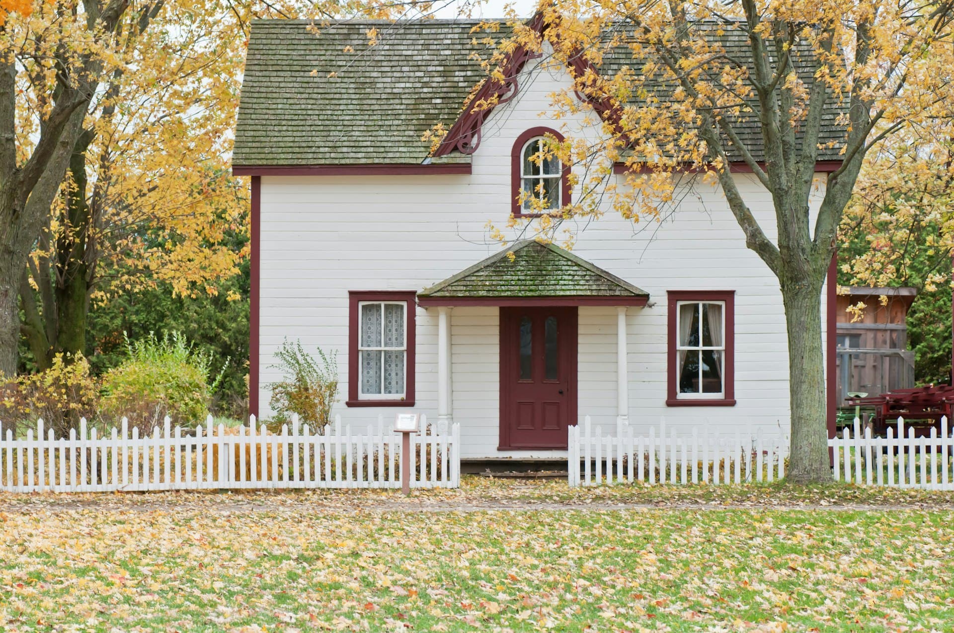 White clapboard family home with a picket fence under autumn trees