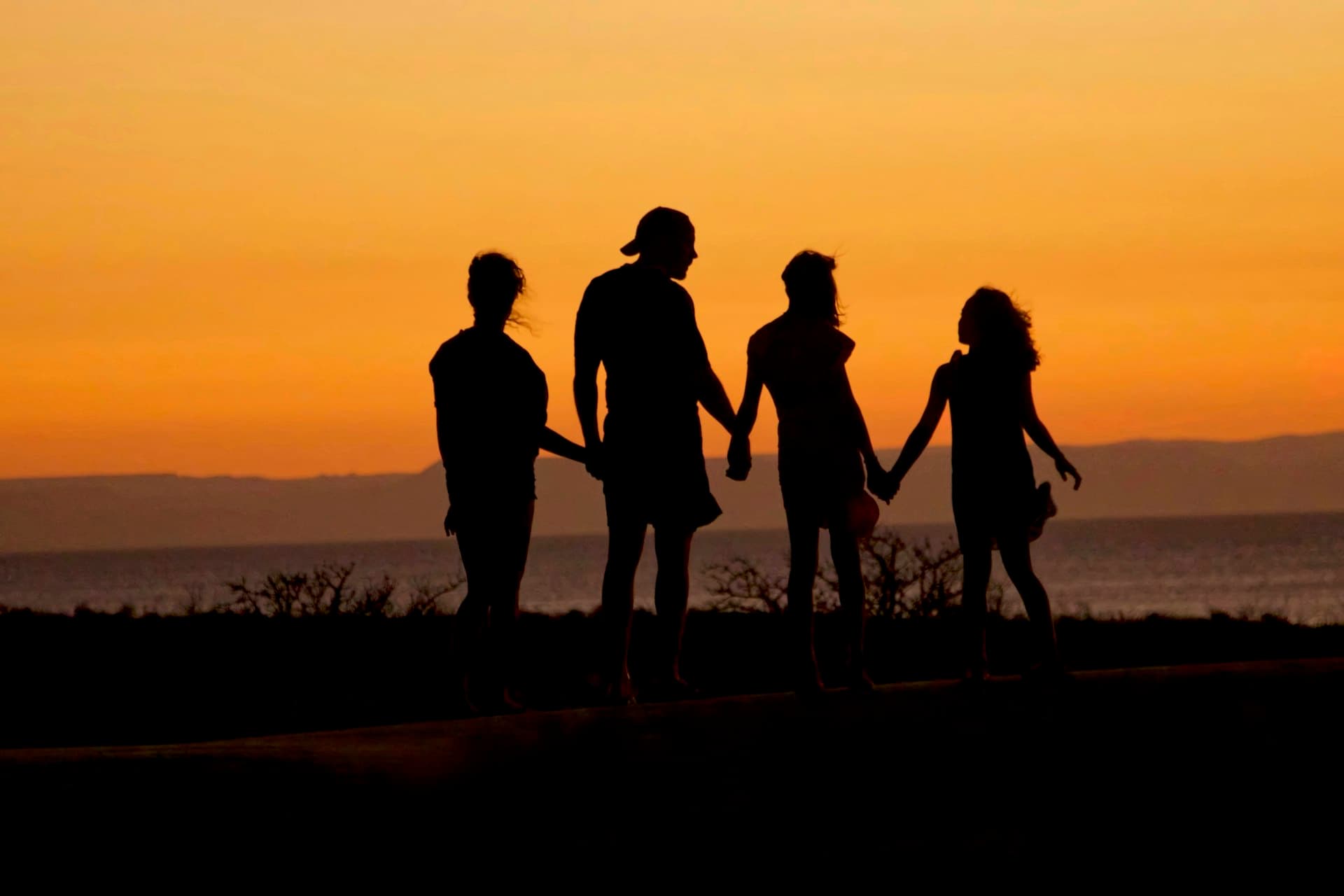 Family of four walking hand in hand along the water at sunset