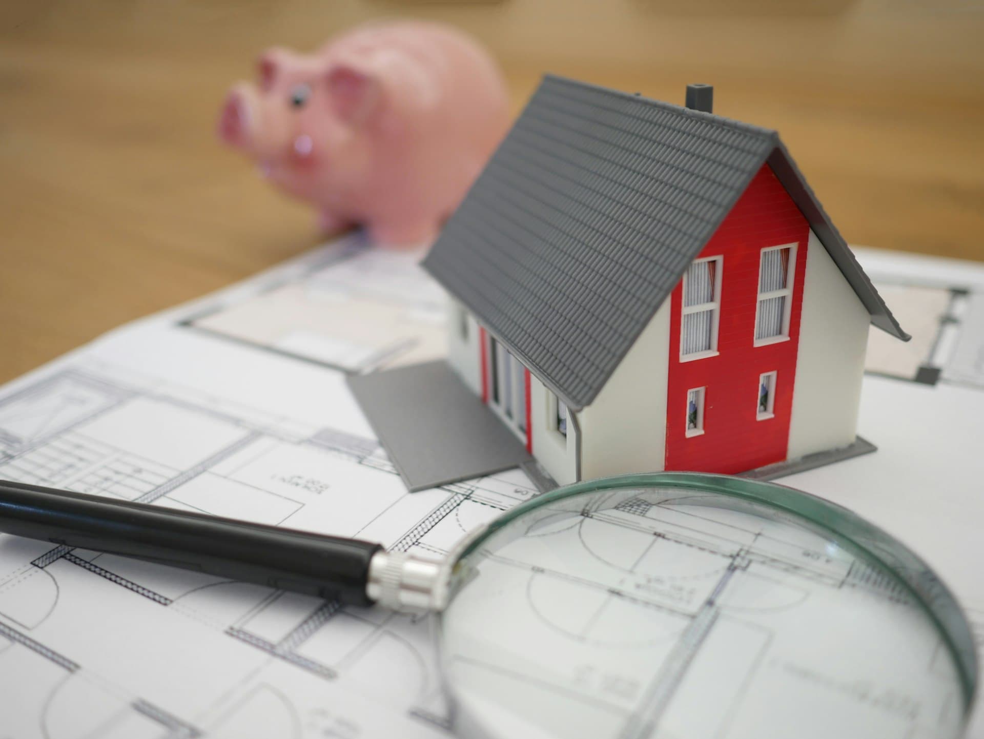 House model, piggy bank, floor plans and magnifier arranged on a desk, representing the details of estate planning