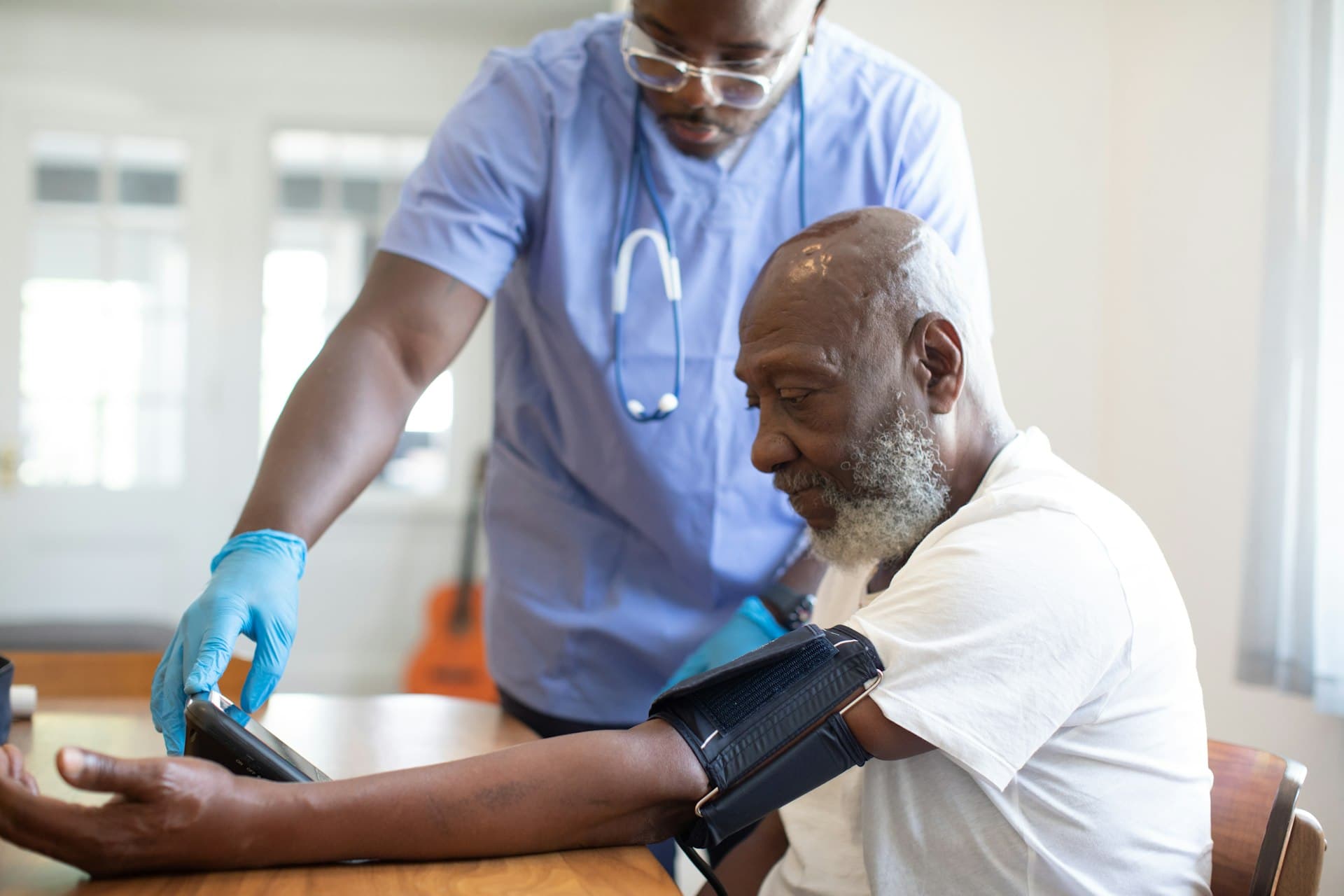 Caregiver in scrubs taking blood pressure of an elderly man at home — elder care and Medicaid planning
