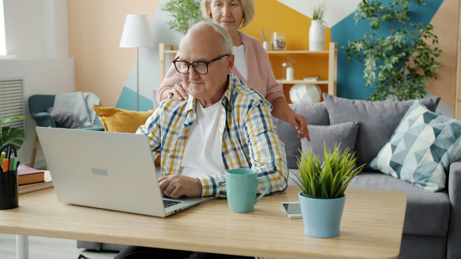 Elderly man seated at a laptop with his wife supportively at his shoulder, representing the families these estate planning scenarios serve