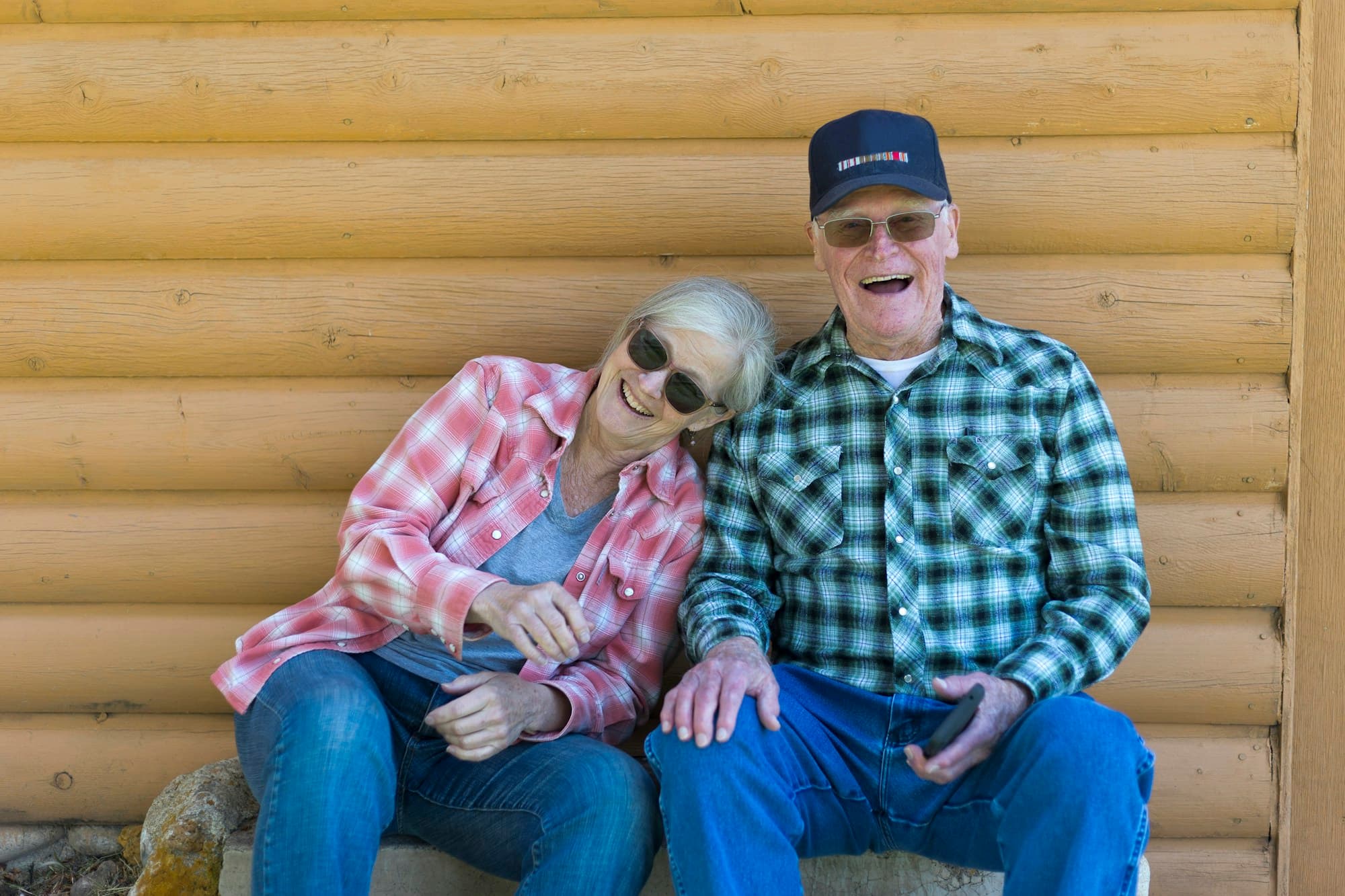 Older couple laughing together on a log-cabin bench in warm afternoon light