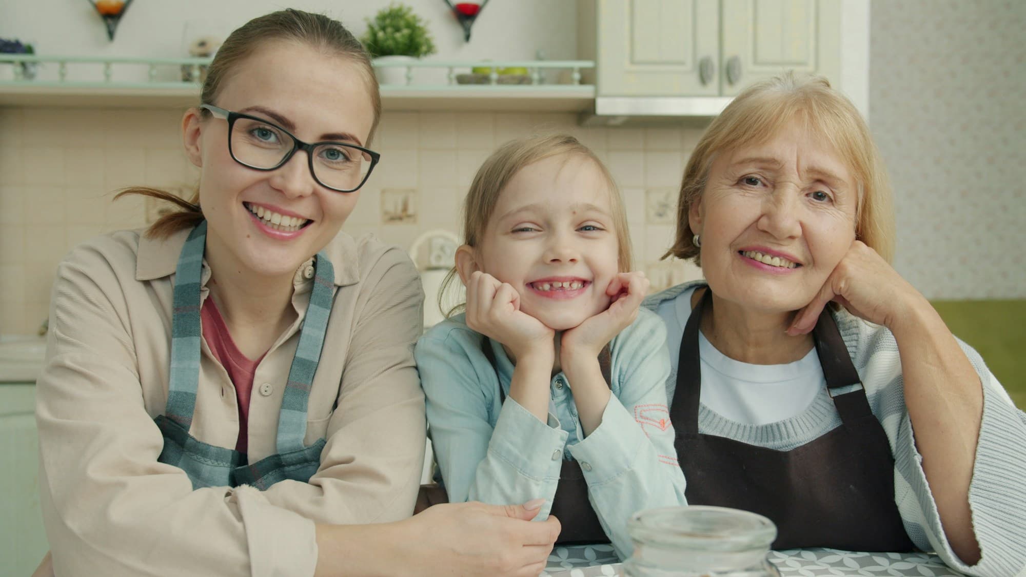 Three generations of women smiling together in a sunlit kitchen